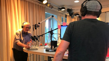 Zwei Männer stehen in einem Radiostudio vor Mikrofonen und Bildschirmen.