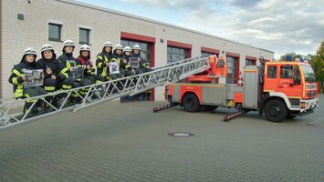 Feuerwehrleute auf Leiter mit Fotos neben einem Feuerwehrwagen