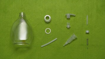 Einzelteile eines Seifenspenders liegen auf einem grünen Untergrund