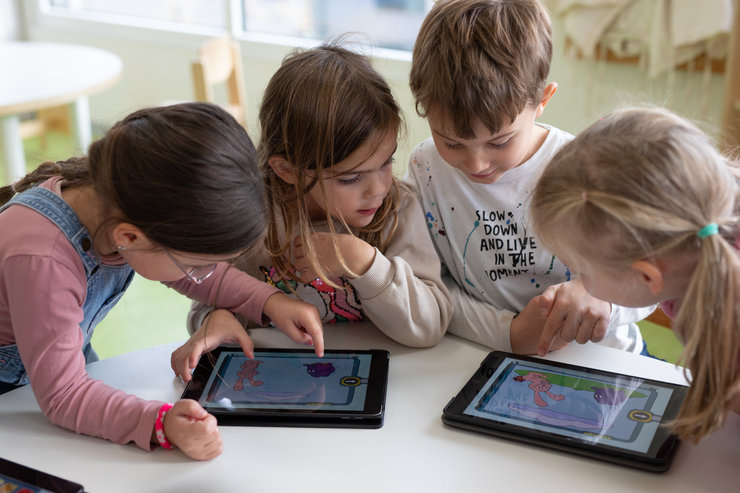 Vier Kinder am Tisch über Tablets mit der Wenn-Dann-Maschine gebeugt