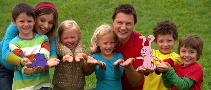 Tanja und André schauen mit fünf Kindern in die Kamera und tragen Elefant und Hase auf den Händen