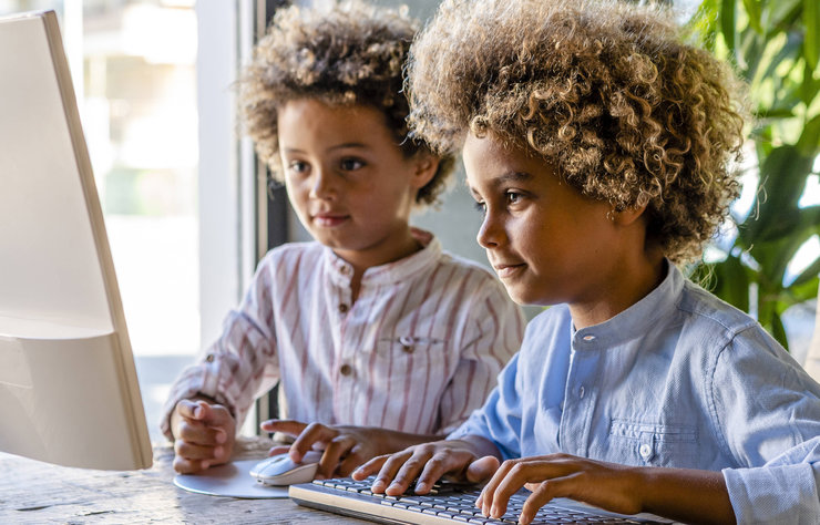 Zwei Kinder nebeneinander vor einem Computer mit Maus und Tastatur