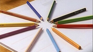 Buntstifte liegen sternenfï¿½rmig auf einem Blatt Papier auf einem Tisch.