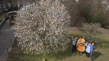 Andre, die Maus, und ein Ehepaar stehen neben einem Baum, der mit Ostereiern geschmückt ist