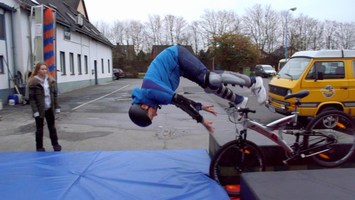 Johannes macht einen Fahrrad-Stunt über einer blauen Matte