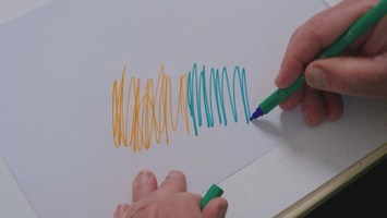 Ein grüner Filzstift malt auf einem weißen Blatt Papier.
