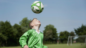 Ein Junge spielt alleine Fußball und trainiert Kopfbälle