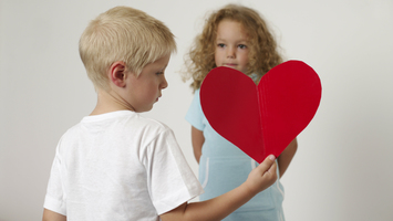 Ein Junge steht mit einem roten Herz vor einem Mädchen