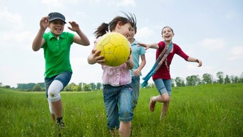 Kinder toben mit einem Ball über die Wiese
