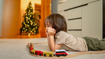 Ein Junge liegt nachdenklich auf dem Teppich vor einem Weihnachtsbaum