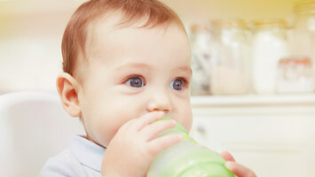 Ein Baby mit blauen Augen trinkt aus einer Flasche.