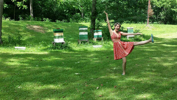 Eine Frau steht vor Bienenstöcken und reckt die Beine hoch.