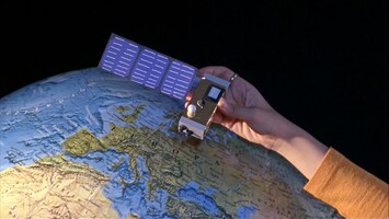 Eine Hand hält einen Mini-Satelliten über ein Modell der Erde
