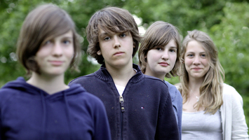 Vier Teenager stehen in einer Reihe hintereinander und schauen in die Kamera