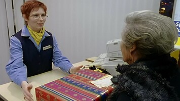 Frau übergibt Weihnachtspaket an Postbeamte. Die beiden Frauen schauen sich an.