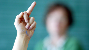 Kind in der Schule zeigt Lehrerin im Hintergrund den Mittelfinger