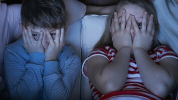Zwei Kinder halten sich beim Fernsehgucken die Hände vor die Augen