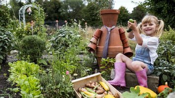 Smiling blond girl sitting in garden next to terracotta