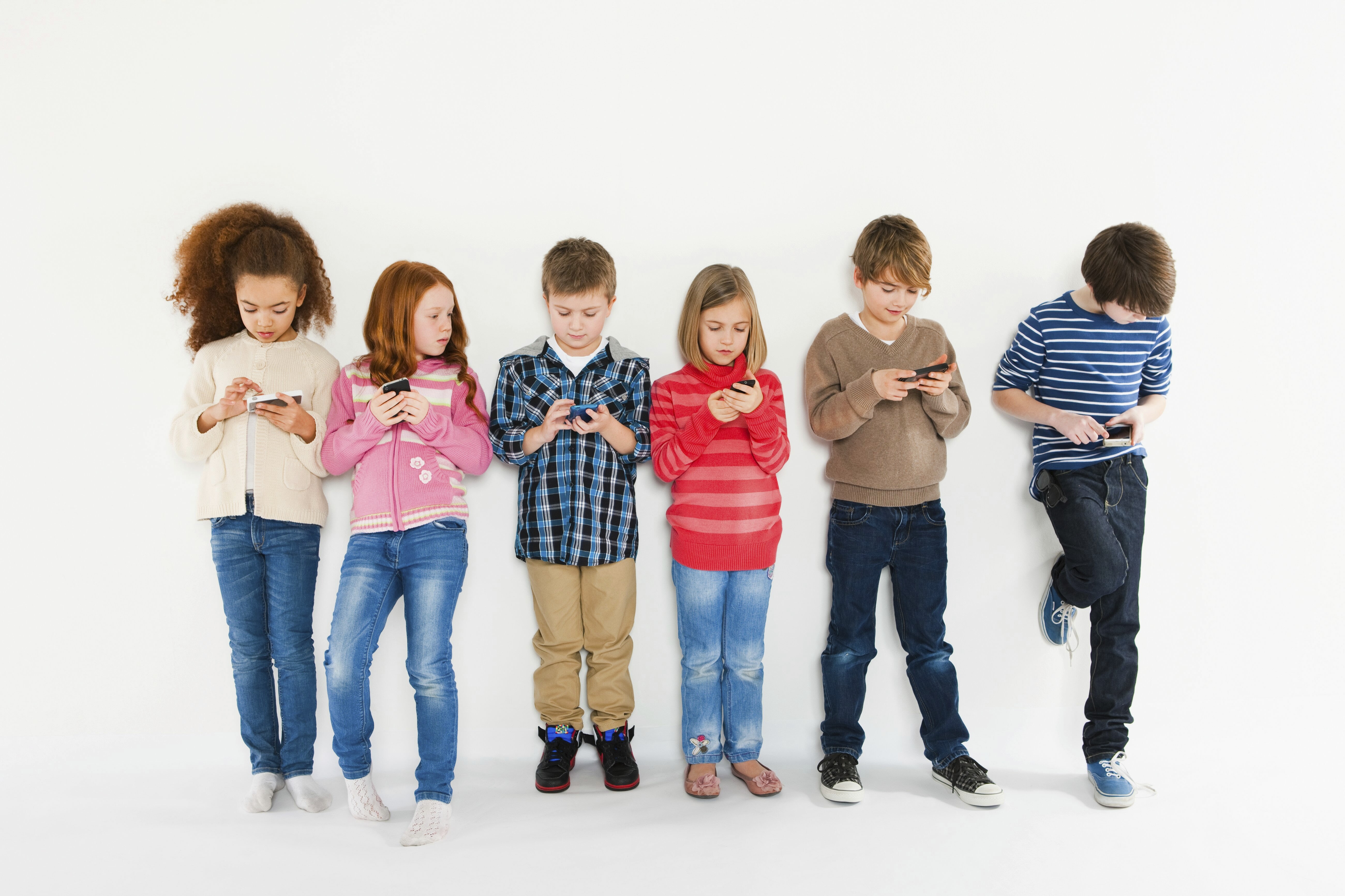 Sechs Kinder stehen nebeneinander und spielen mit ihren Smartphones.