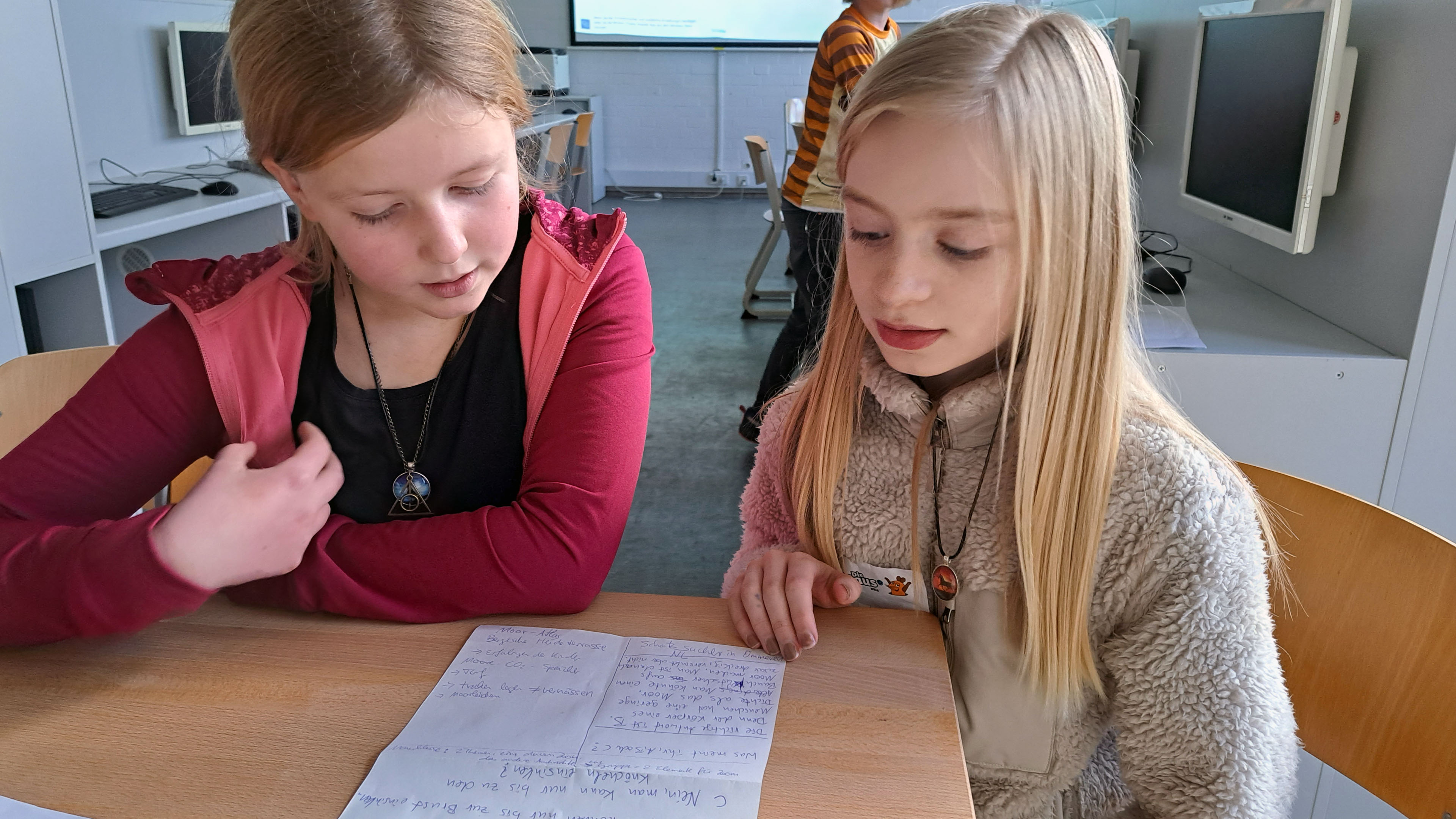 Zwei Mädchen sitzen vor einem Zettel mit Notizen