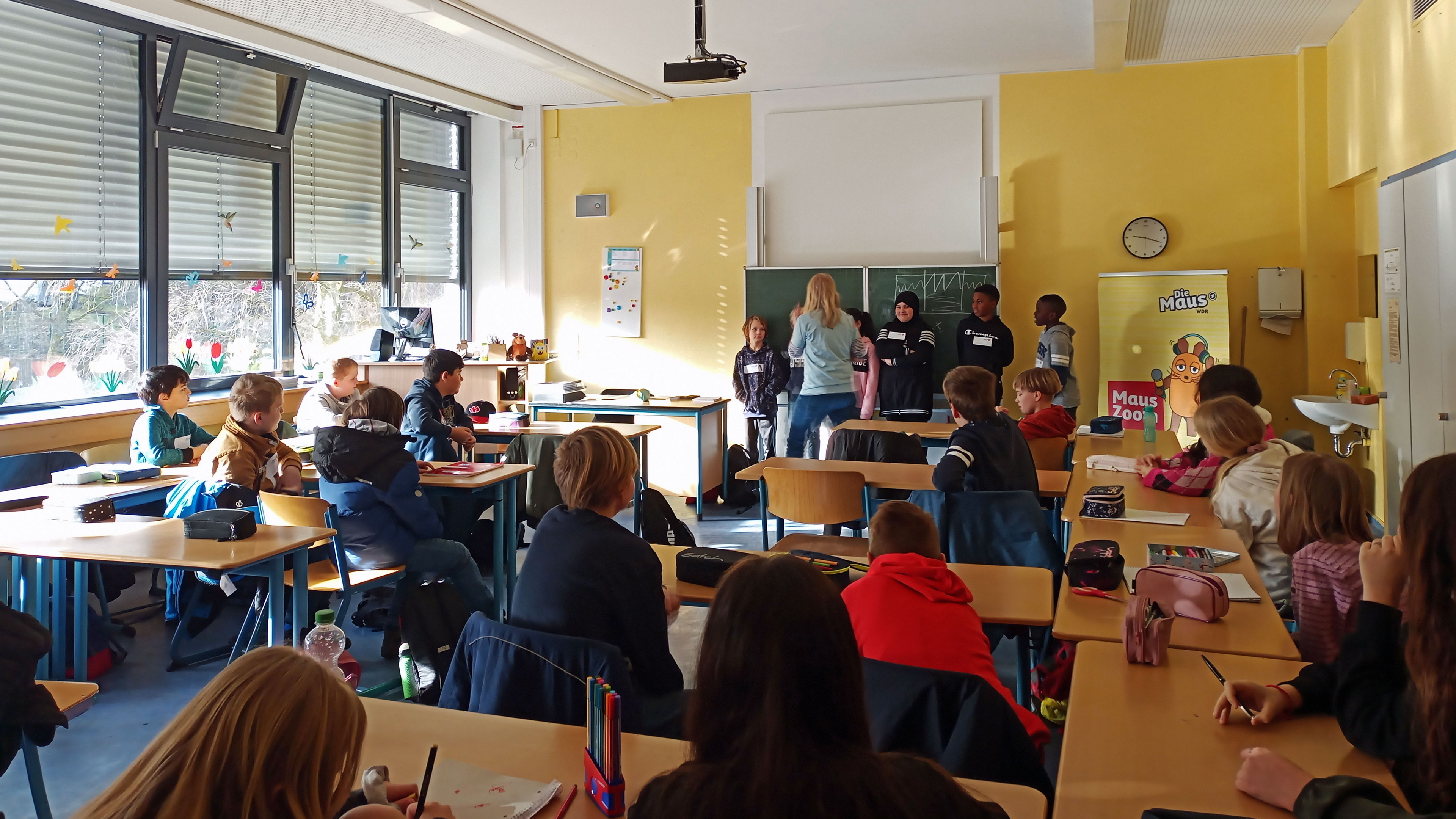 Schülerinnen und Schüler werden in ihrer Klasse von einer Reporterin interviewt.