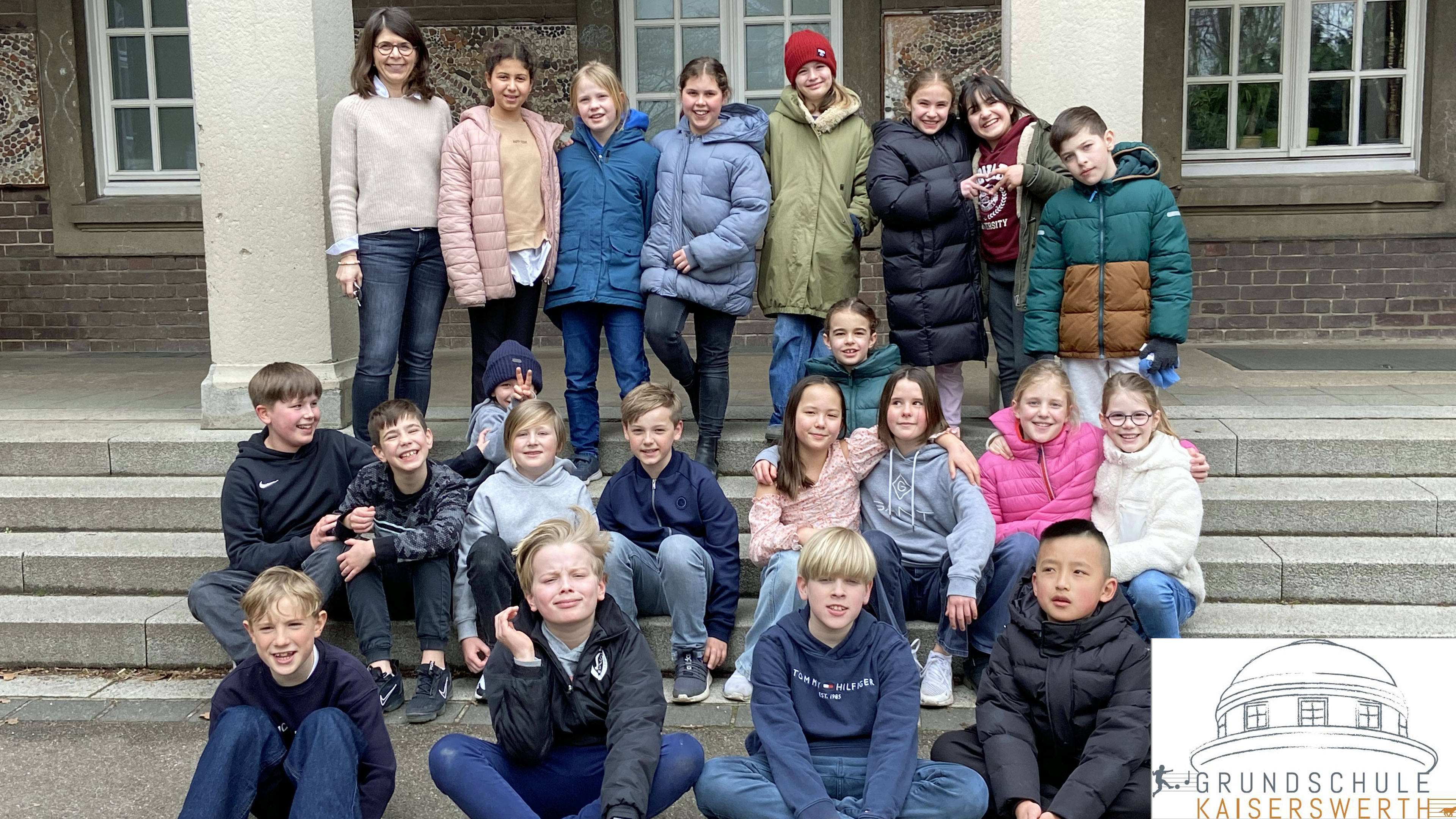 Bildrechte: WDR / Grundschule Kaiserswerth Düsseldorf Eine Schulklasse sitzt und steht vor dem Eingang ihrer Schule.