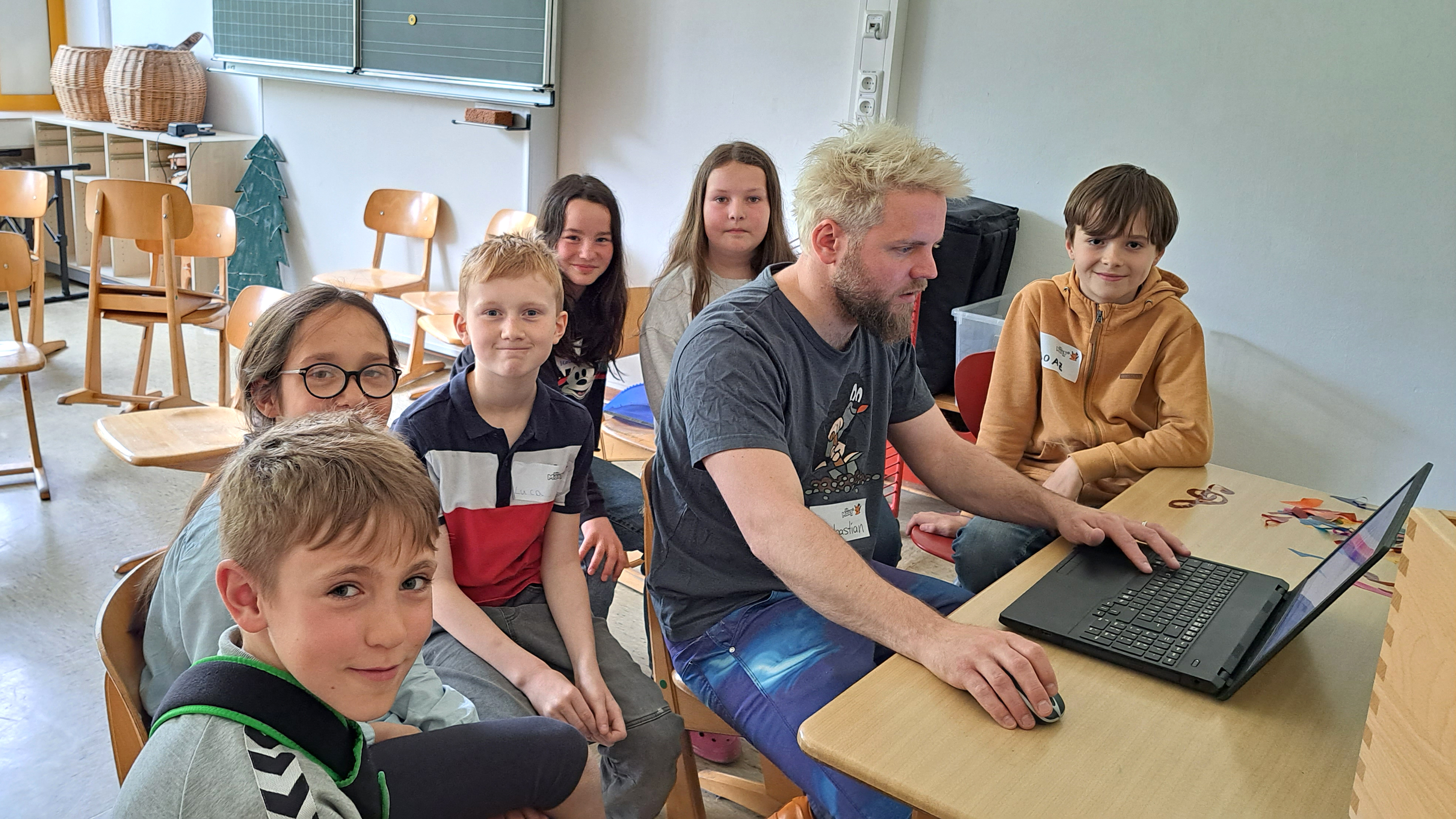 Kinder der MausKlasse schauen MausZoom-Reporter Sebastian dabei zu wie er die MausZoom-Aufnahme am Computer bearbeitet