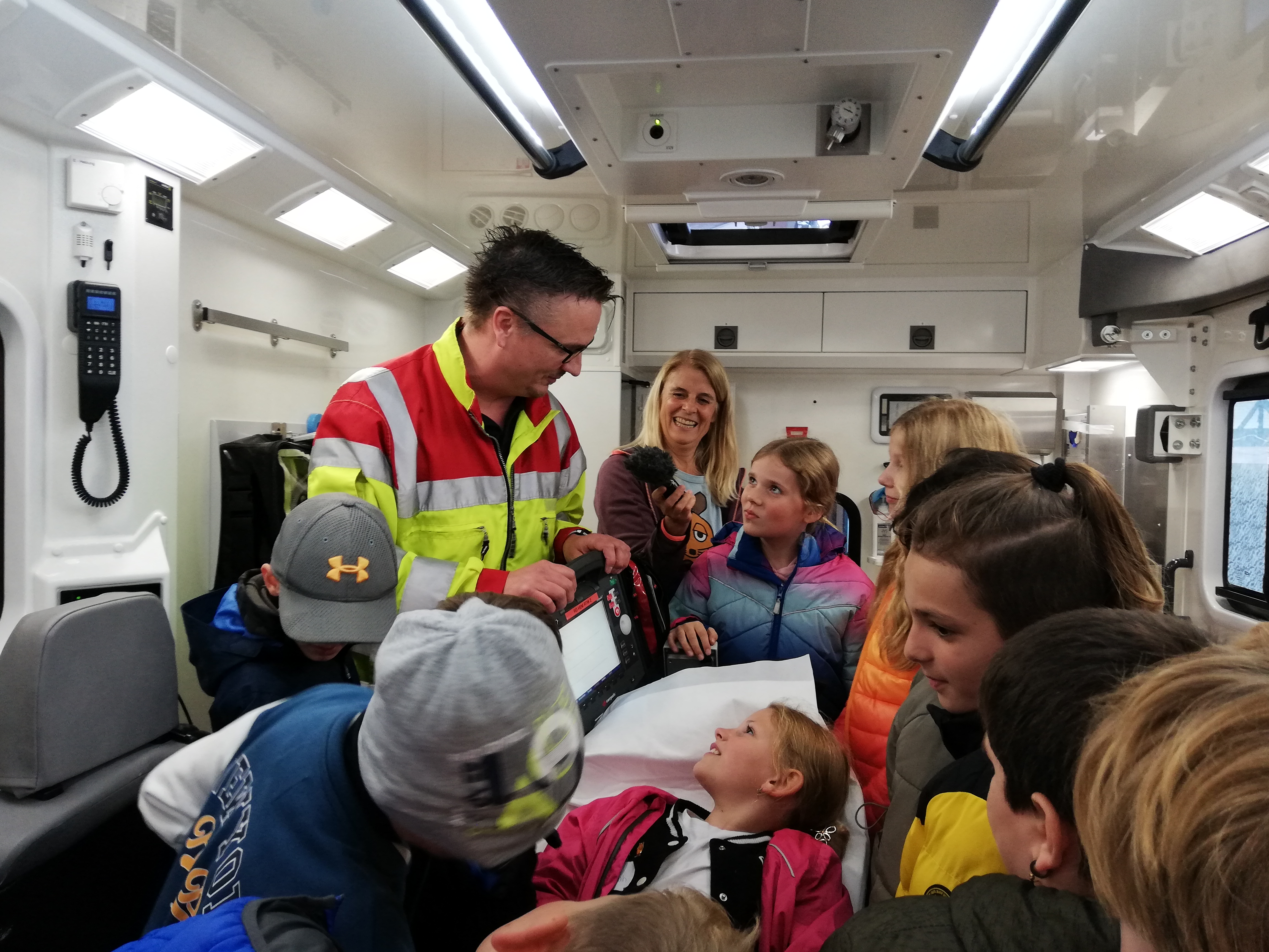 Eine Schulklasse steht mit einem Rettungssanitäter in einem Rettungswagen.