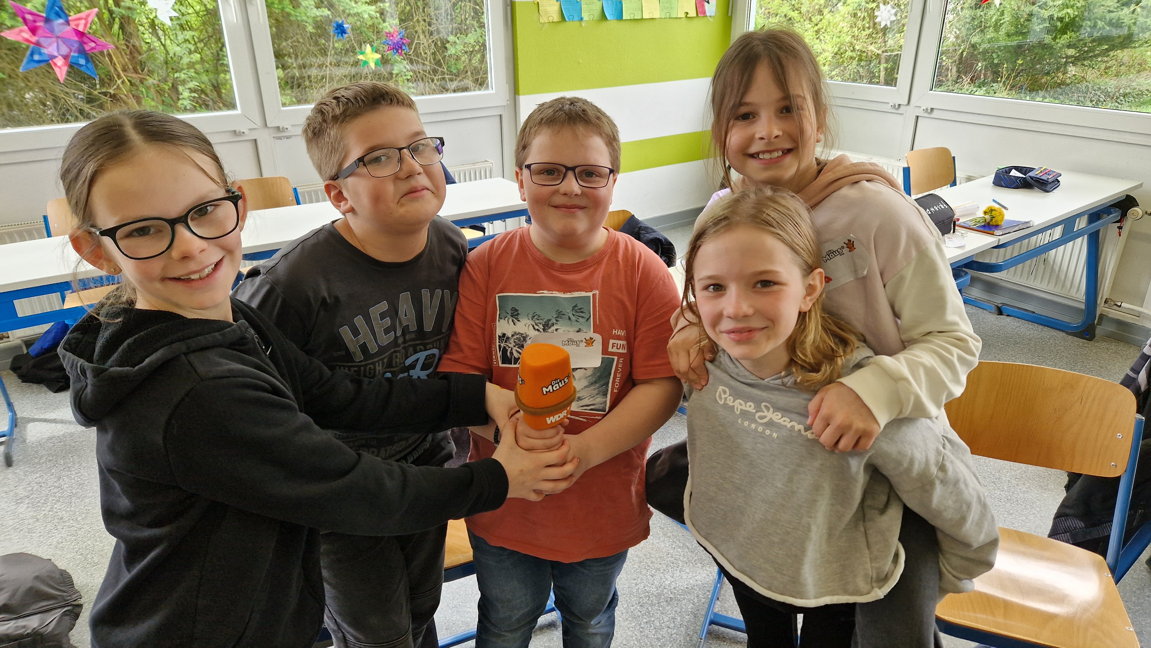 Kinder stehen zusammen und halten ein orangenes Mikrofon in der Hand.