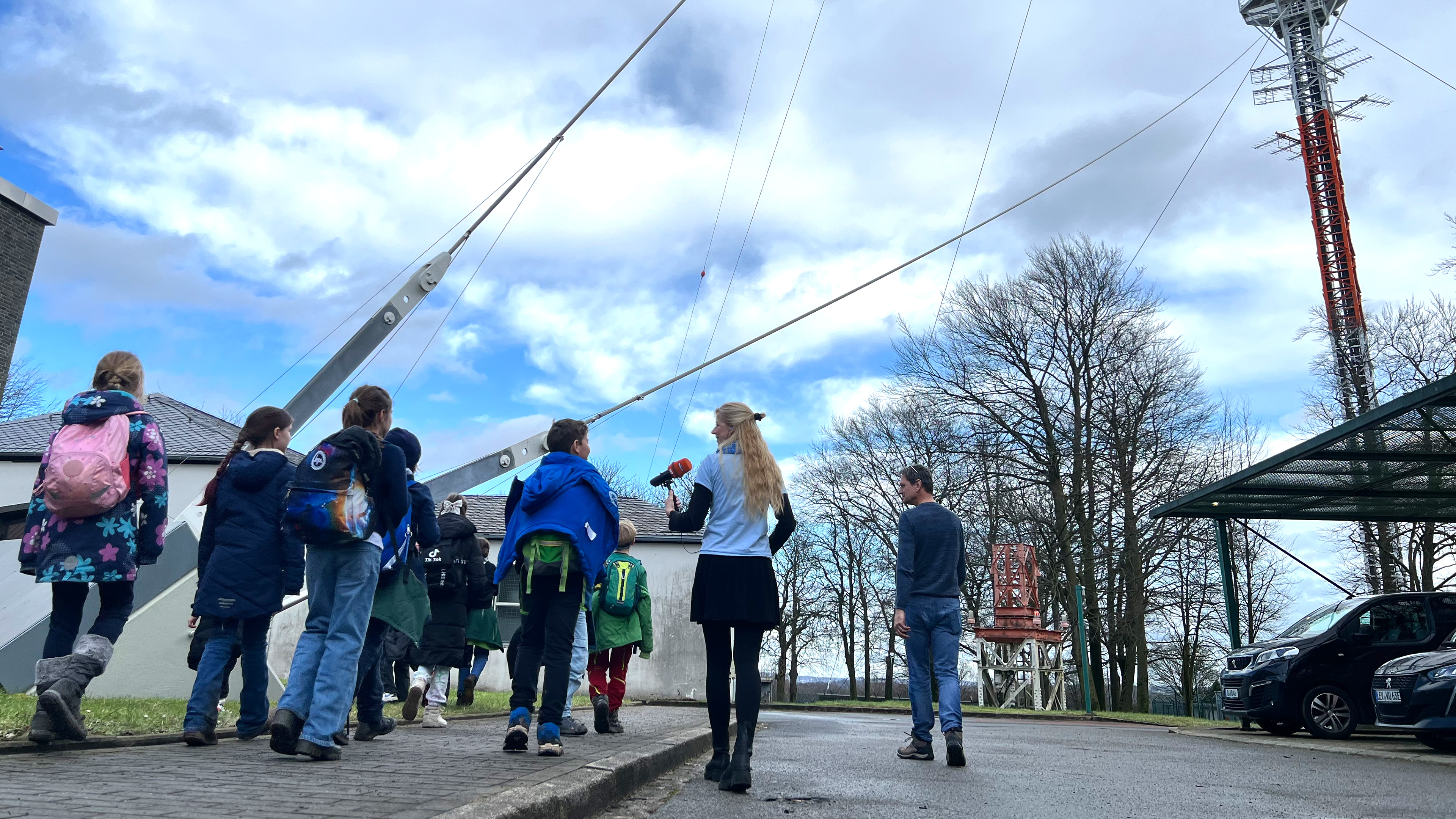 Kinder MausKlasse laufen mit Reporterin Insa auf einer Straße, im Hintergrund der Sendemast des Senders Langenberg