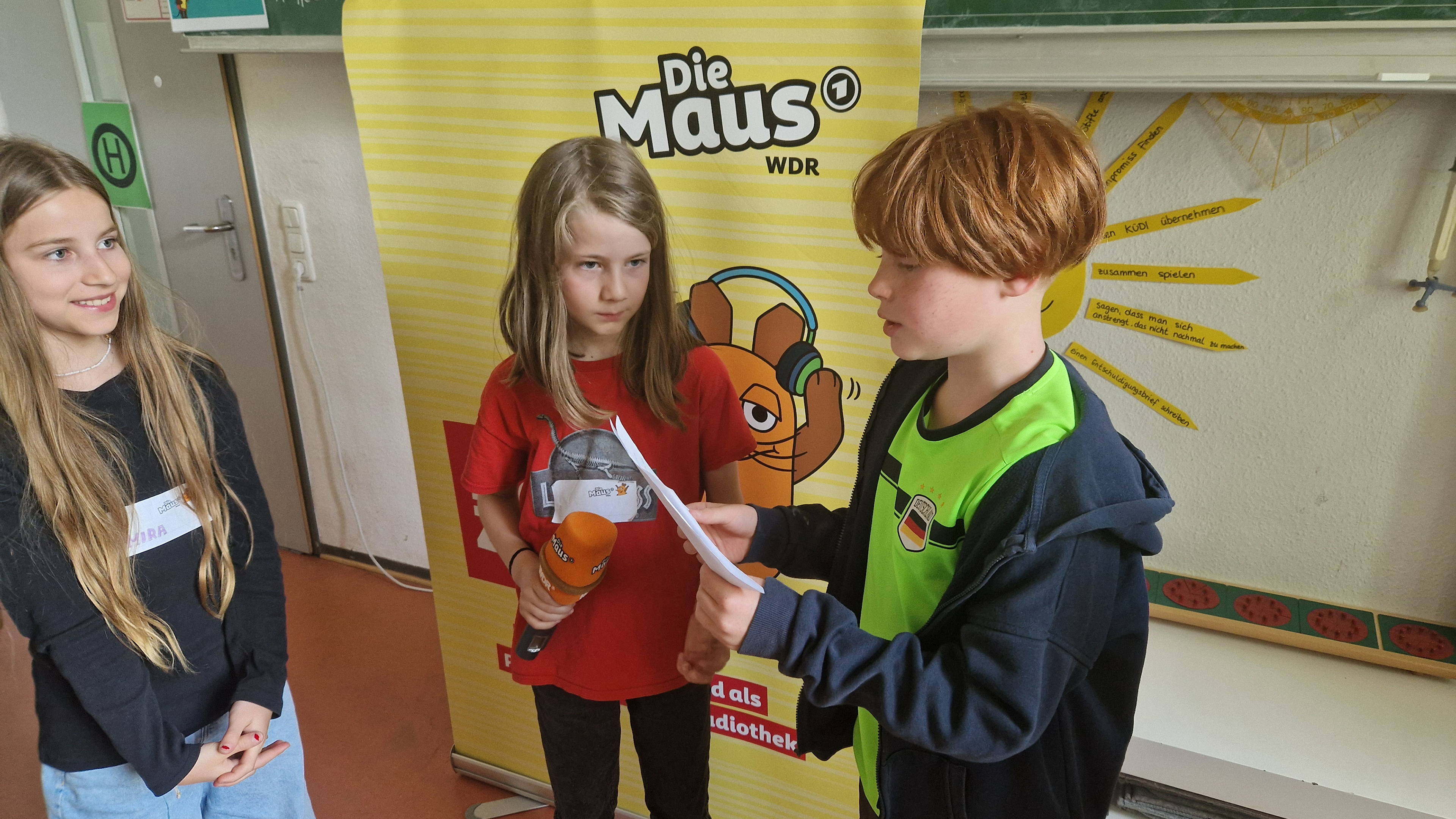 Drei Kinder der MausKlasse mit Maus-Mikrofon in ihrem Klassenzimmer