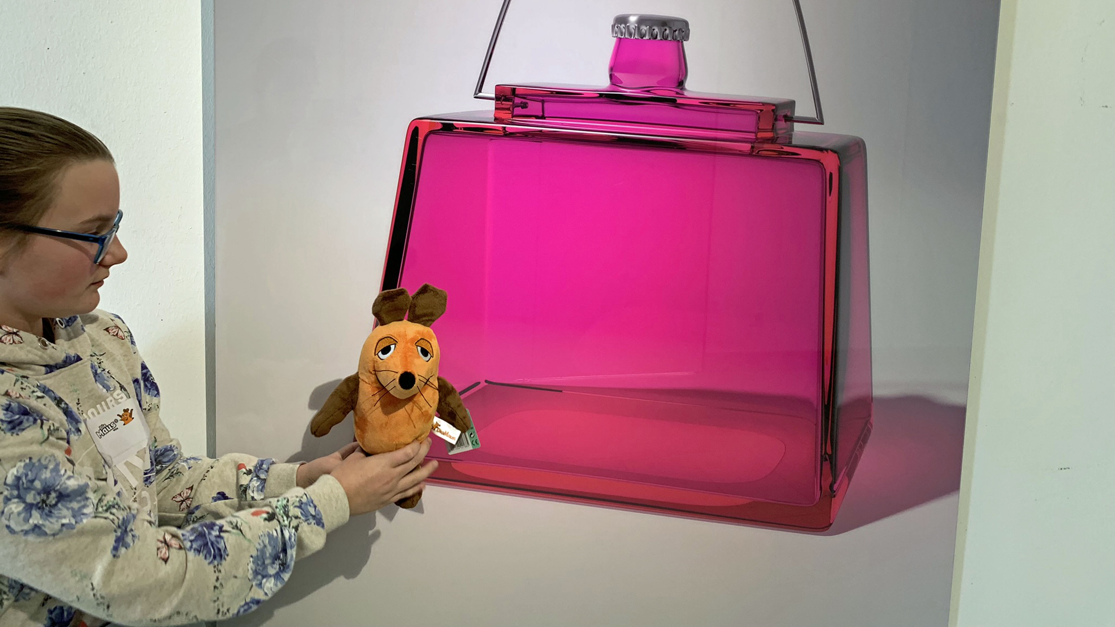 Eine pinke Handtasche aus Glas und ein Mädchen hält die Maus in der Hand.