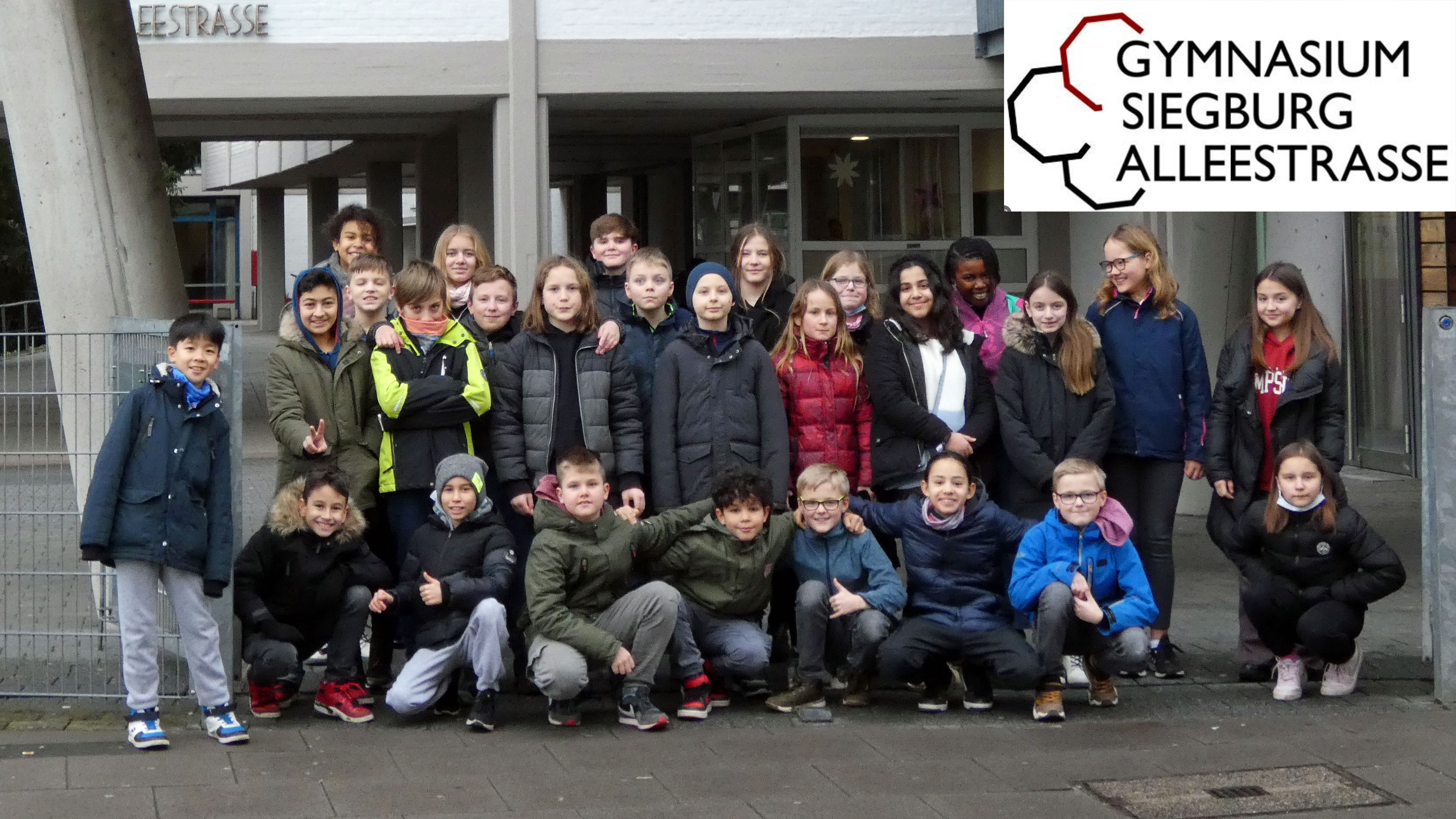 Eine Schulklasse mit Mädchen und Jungen steht vor einer Schule.