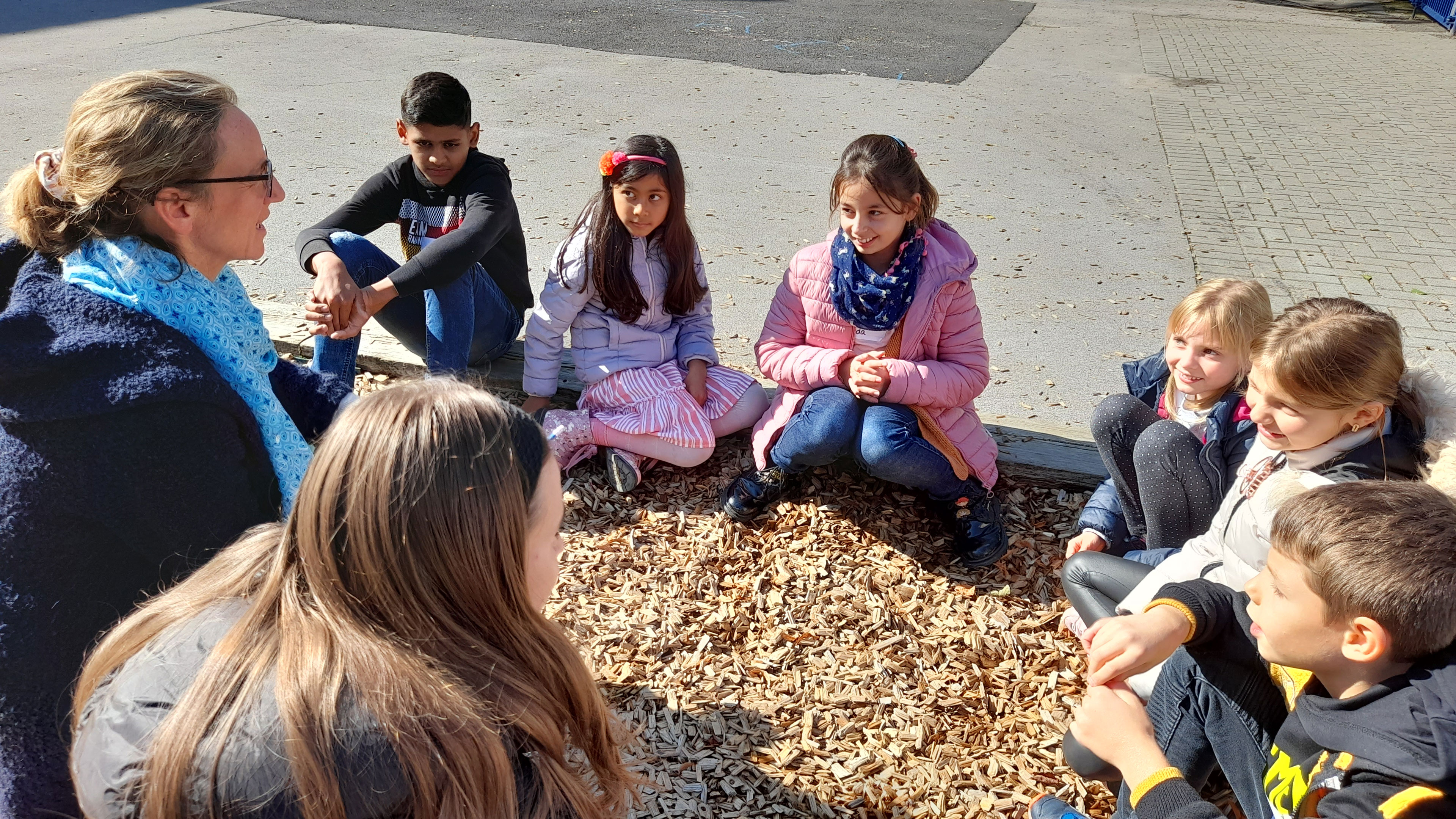Eine Gruppe von Kindern sitzt draußen auf dem Boden.
