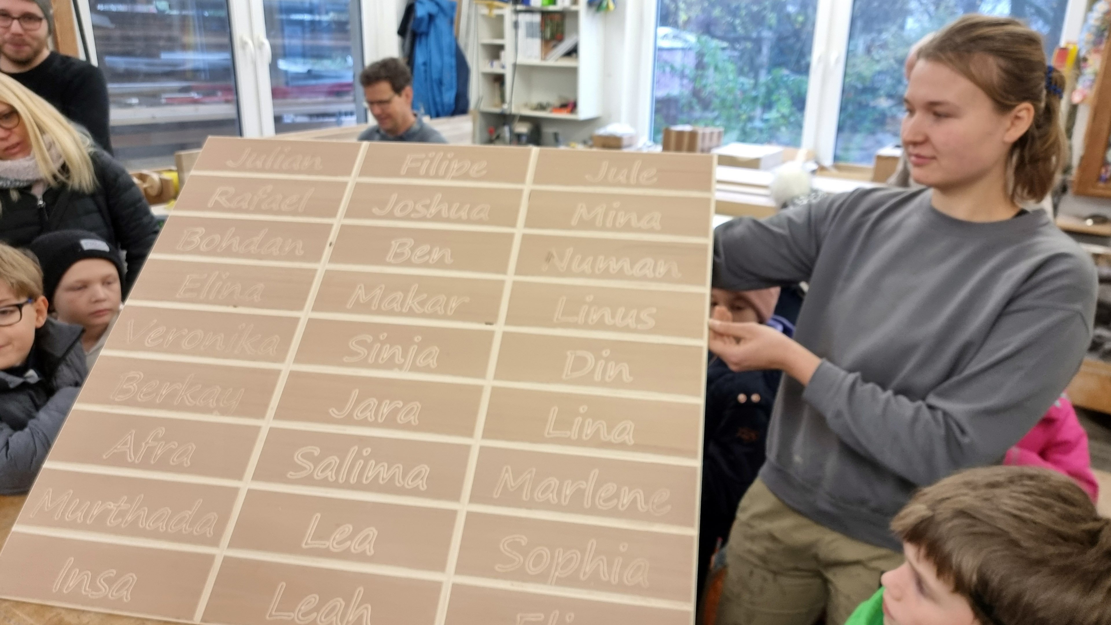 Tischlerin Ines zeigt eine Holzplatte mit den Namen der Kinder darauf