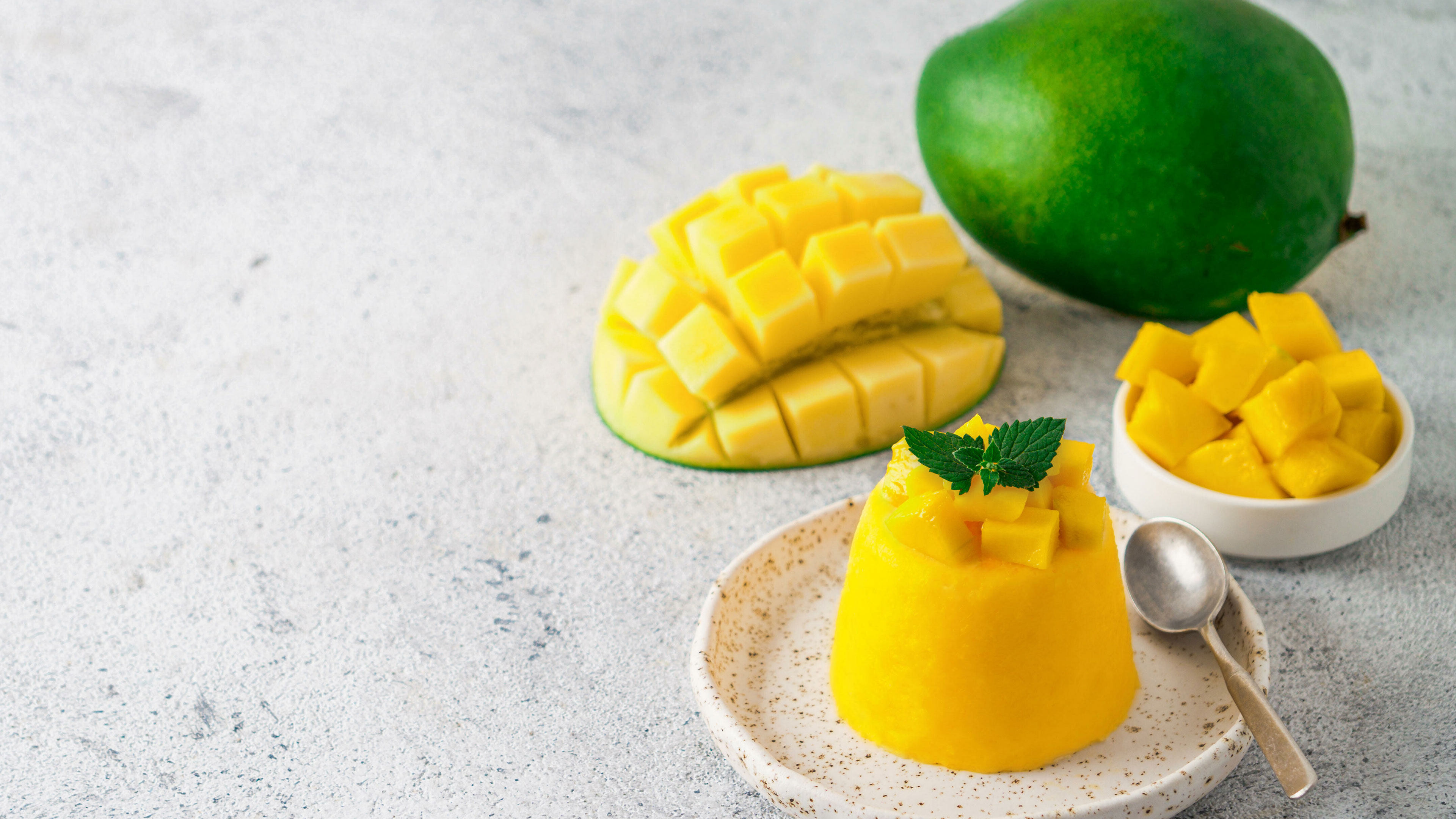 Eine Mango, eine aufgeschnittene Mango und Mango-Mousse stehen auf einem Tisch