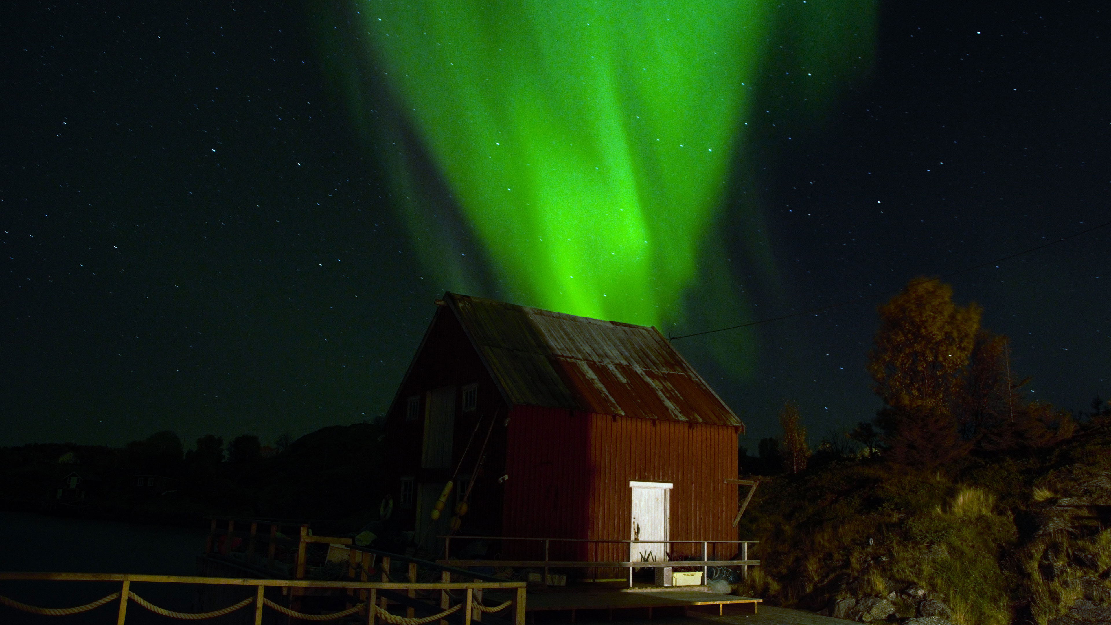 Ein grünes Licht leuchtet am Nachthimmel hinter einer Hütte
