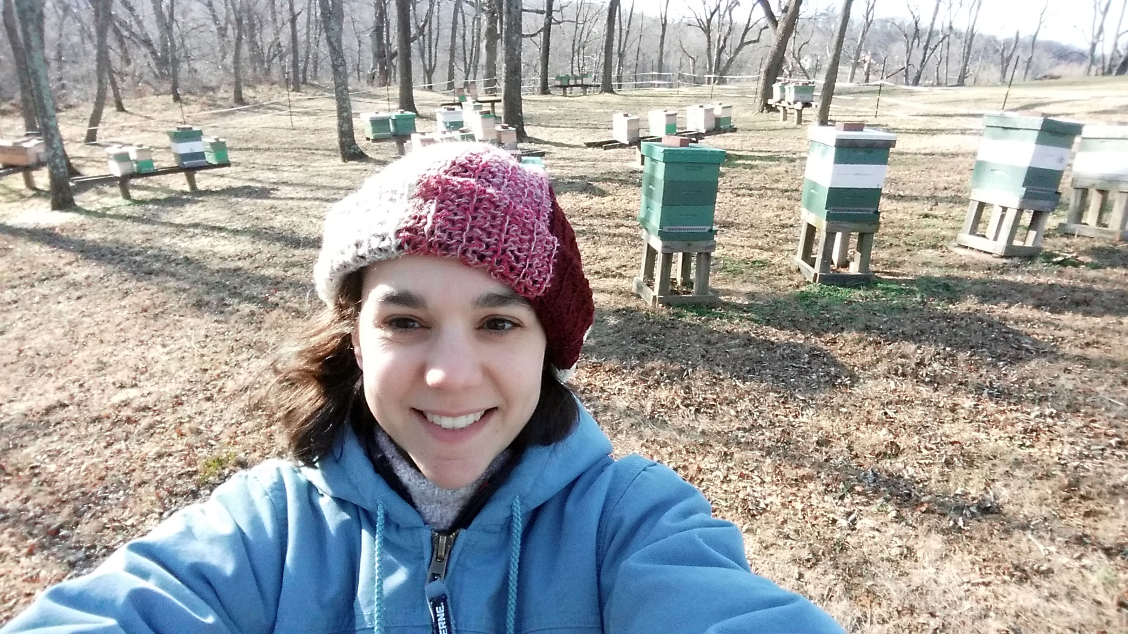 Eine Frau macht ein Selfie vor Bienenstöcken im Wald.