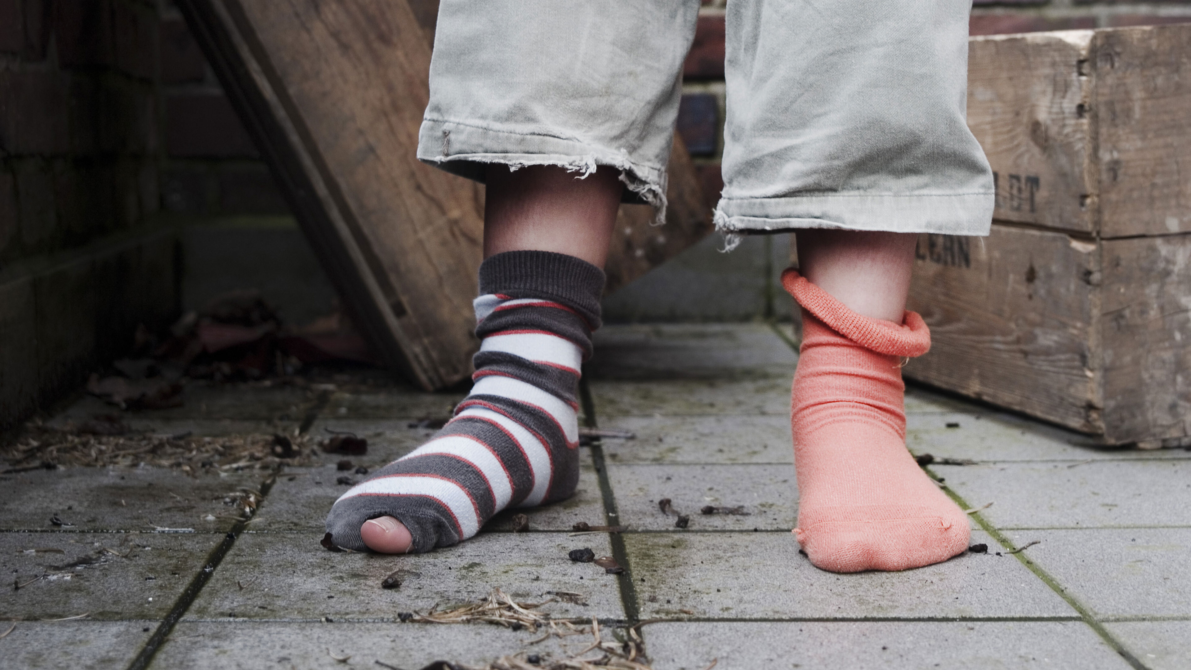 Ein Kind steht mit kaputten Socken auf einer Straße.