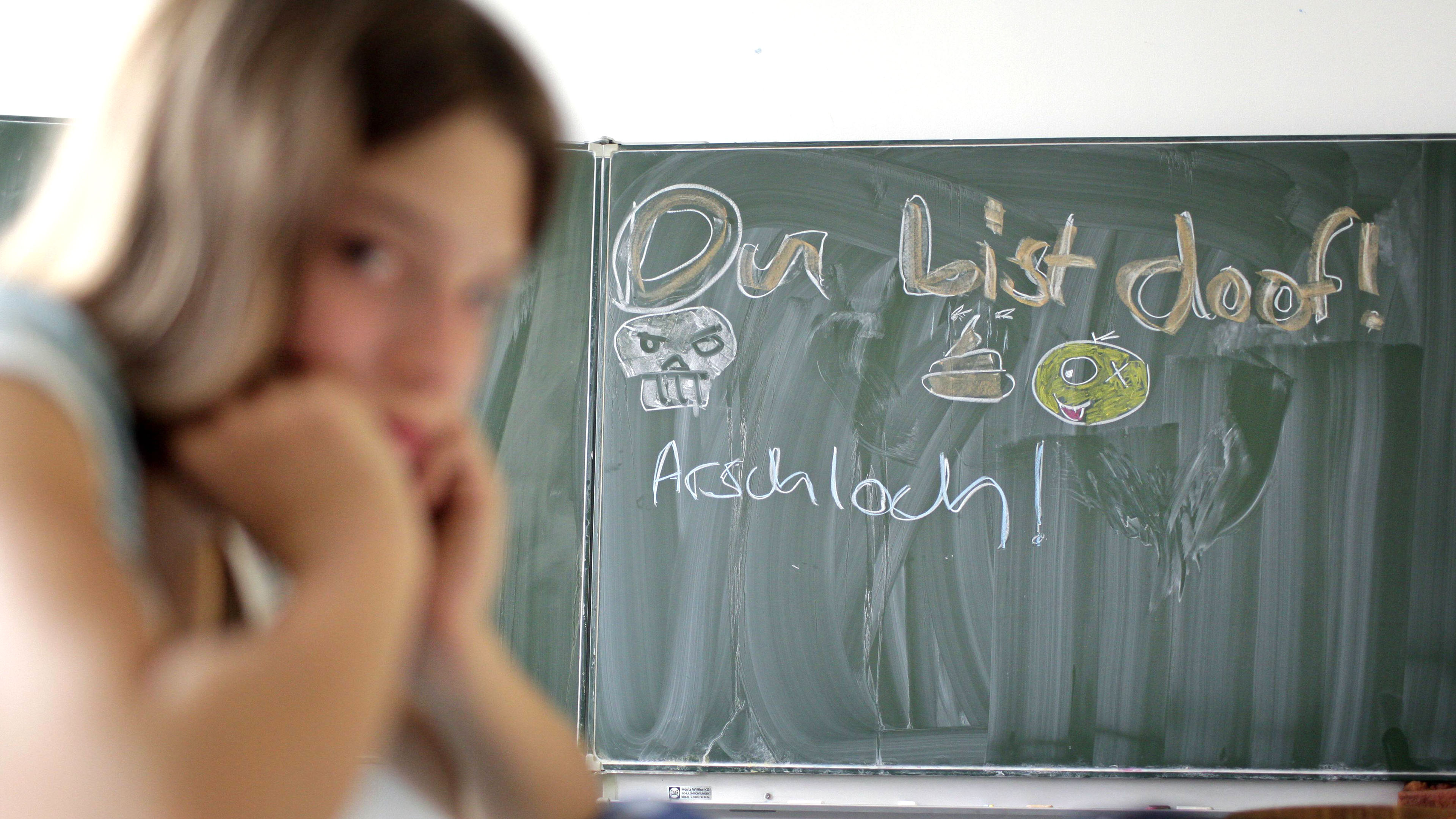 Mädchen vor Schultafel mit Beleidigungen drauf