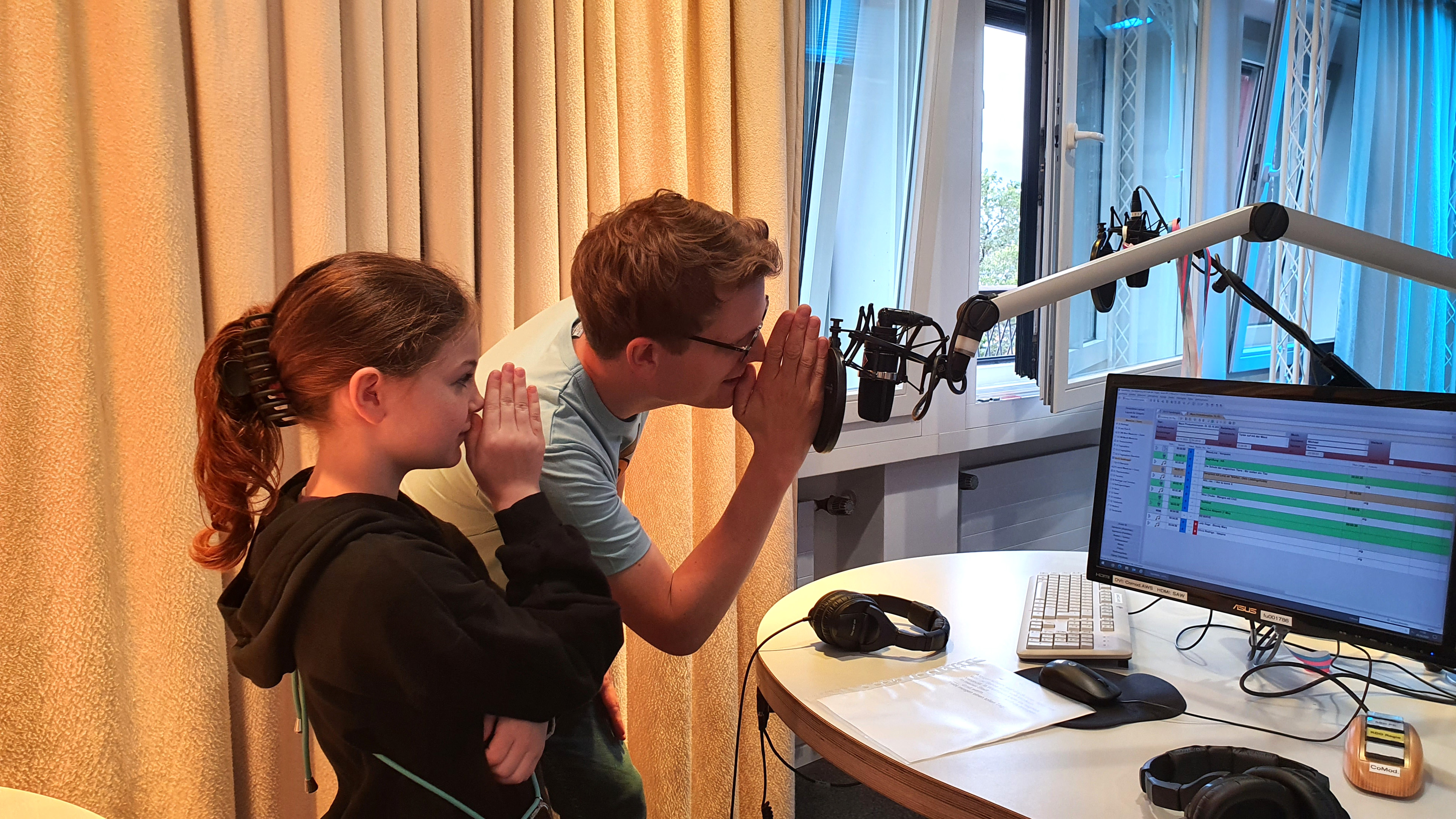 MausLive-Moderator Johannes steht mit einem Mädchen am Mikrofon am MausLive-Sendepult