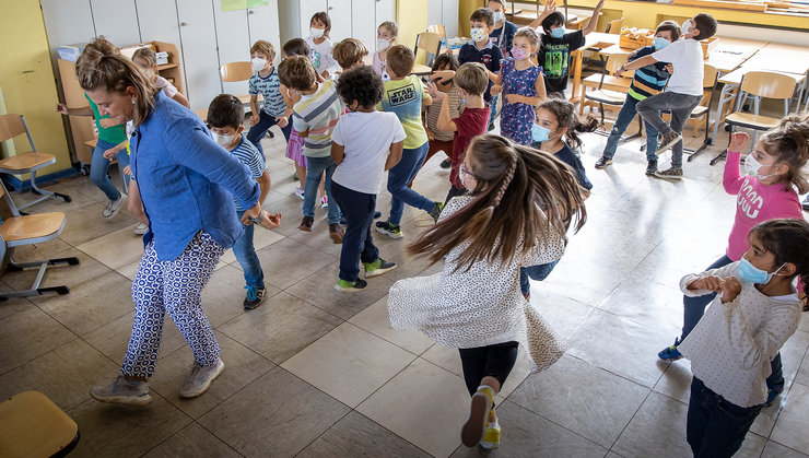Viele Kinder und eine Lehrerin im Klassenzimmer tanzen