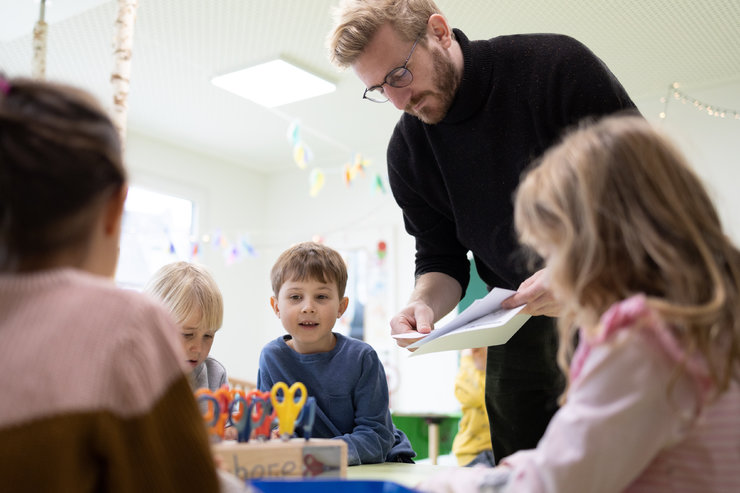 Ein erwachsener Mann teilt Kindern Papiere aus