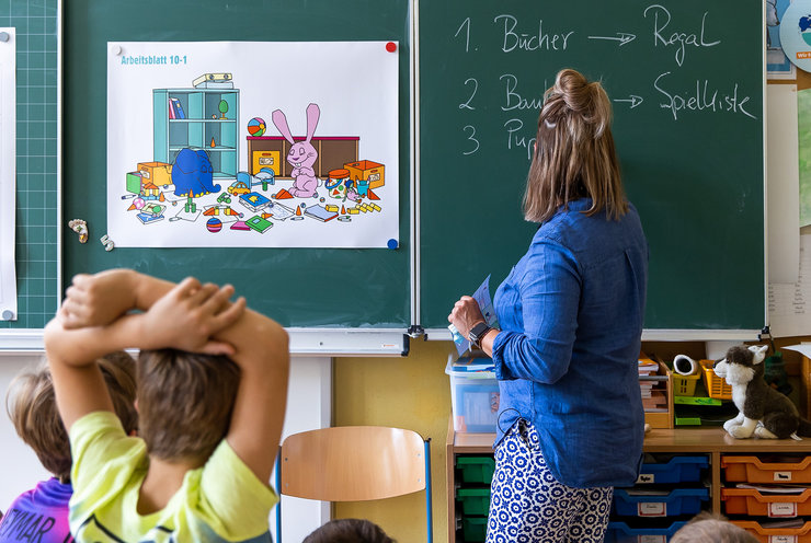 Eine Lehrerin schreibt an die Tafel, einige Kinder von hinten davor