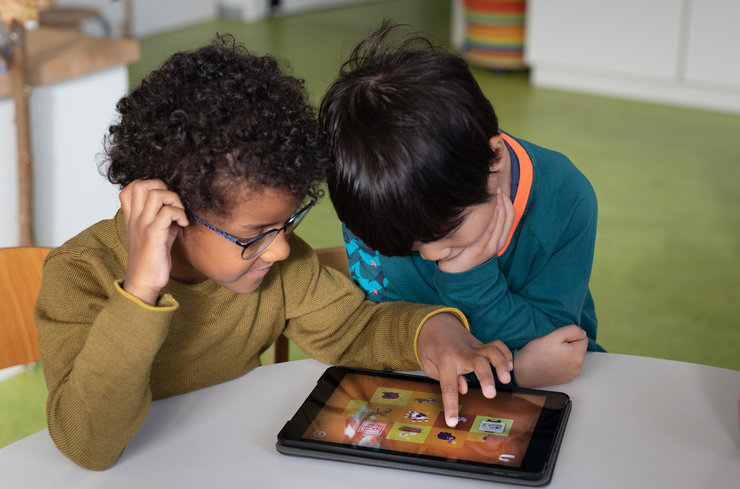 Zwei Kinder sitzen über einen Tablet gebeugt am Tisch