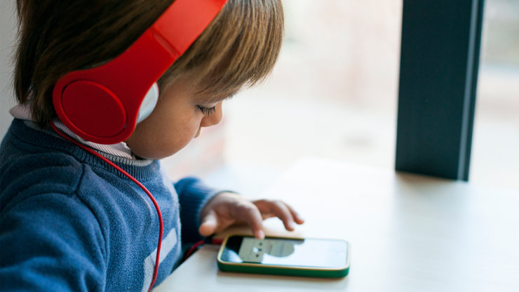 Kind mit roten Kopfhörern vor einen Smartphone 