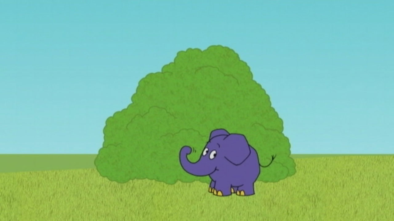 Der Elefant steht vor einem Busch und hebt seinen Rüssel
