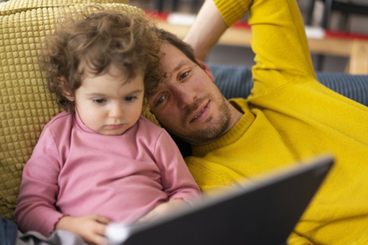 Vater und kleine Tochter sitzen auf dem Sofa und schauen in einen Laptop