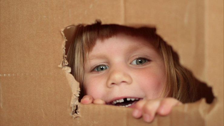 Mädchen schaut aus einem Loch im Karton