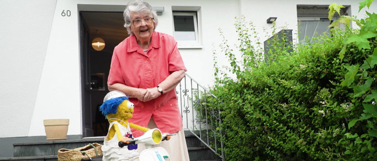 Puppe Biene und ältere Frau stehen vor einem Haus